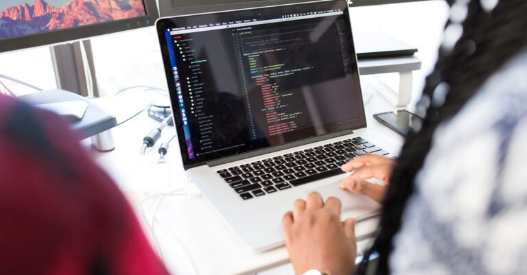 A woman coding on a laptop in a modern office environment with multiple monitors.